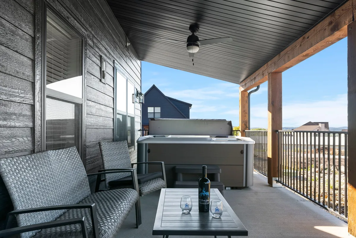 An inviting private patio featuring a hot tub, outdoor seating, and a bottle of wine, with a scenic view visible in the background. The mood is serene and perfect for unwinding after an adventurous day.