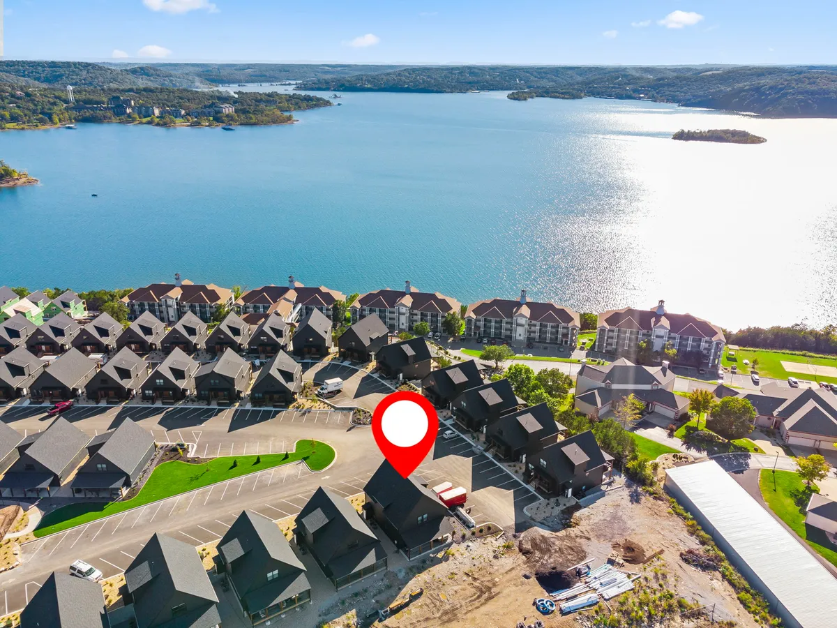 An exterior perspective offering a wide view of the lake, with residential buildings, landscaped green space, and a parking area in the foreground. The scene encompasses both the proximity to the water and the community atmosphere of the neighborhood.