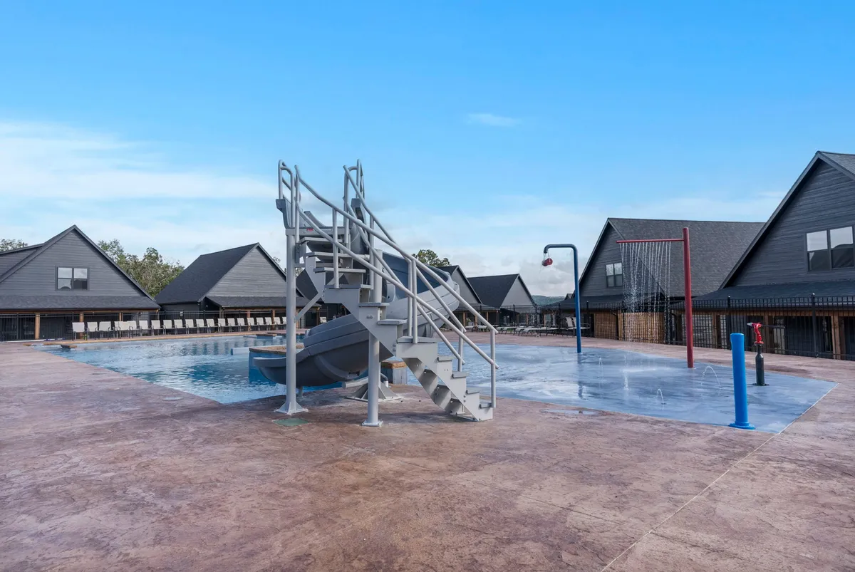 An exterior view of the swimming pool area, featuring a water slide, basketball hoop, and surrounding communal spaces. The pool is set against the backdrop of the retreat's modern construction, suggesting active recreation and community engagement in an eco-conscious environment.
