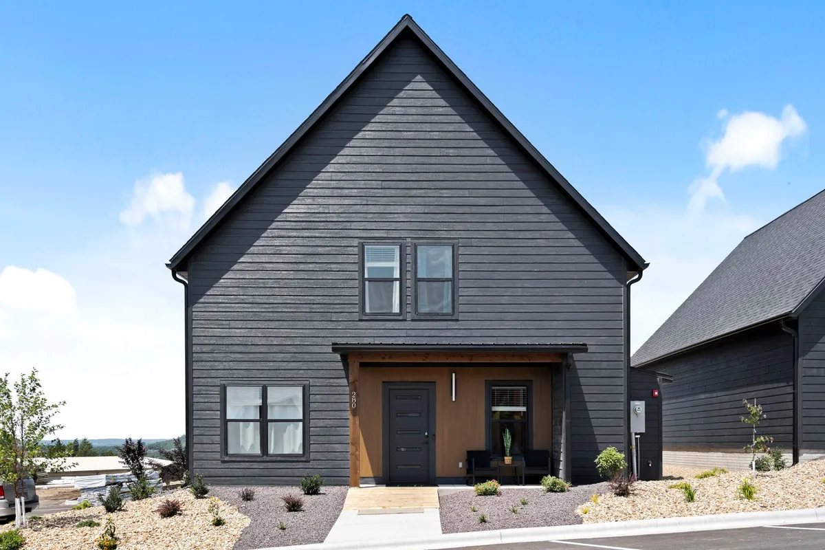 A striking exterior view of the property highlighting dark modern siding, a welcoming wooden front door, and a beautifully landscaped garden. The symmetry of the architecture and the inviting porch set a tone of luxury and attention to detail.