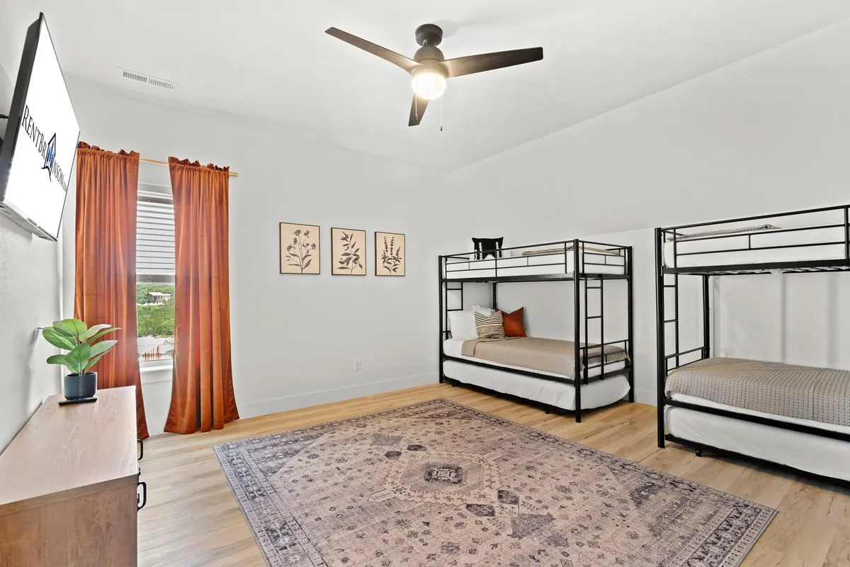 A playful and inviting bunk room with neatly arranged bunk beds, a colorful area rug, curtains, cheerful wall art, and a television. The space is designed for both fun and relaxation, appealing to children and families alike.