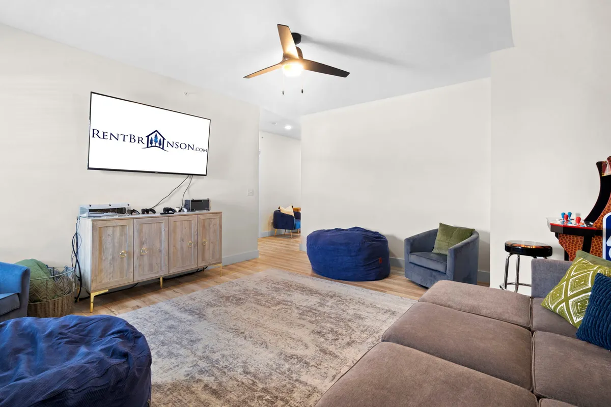 A relaxed entertainment room setup with a large television, plush sofa, bean bags, and a coffee table. The mood is casual and welcoming, designed for group gaming, watching movies, and making memories together.