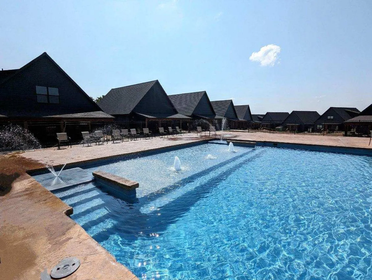 A vibrant outdoor swimming pool surrounded by lounge chairs and fountains with neighboring resort buildings in the background. The scene radiates tranquility and offers a glimpse of the resort lifestyle available to guests.