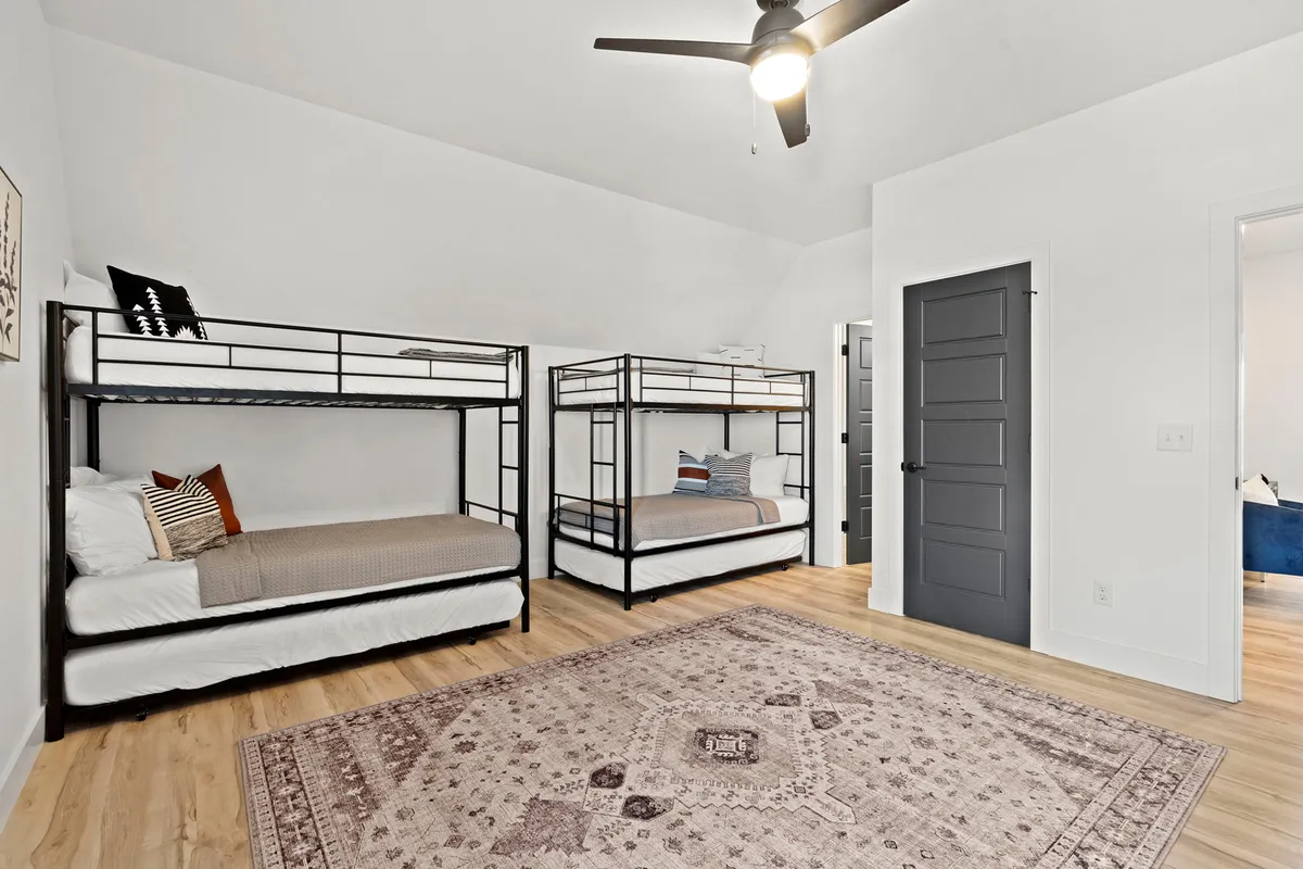 A cozy interior shot of a bunk room designed for children, with multiple bunk beds, a playful area rug, and a ceiling fan. The space radiates warmth and is ideal for late-night chats and shared adventures.