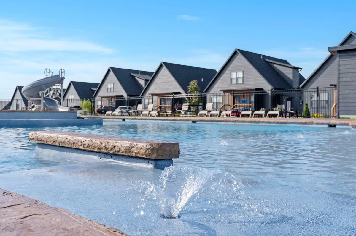 A wide exterior shot of the pool area, complete with a fountain, water slide, and ample space for sunbathing or socializing. The surrounding houses indicate a thoughtfully planned, modern community focused on comfort and sustainability.
