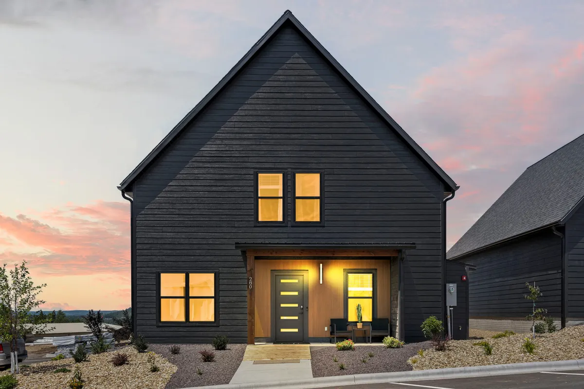 This exterior image features the inviting front door and windows of Rocky Shores Retreat, complemented by lush landscaping. The scene suggests a perfect gathering spot, with ample space on the porch for relaxing or hosting social occasions like barbecues, while the garden adds to the tranquil, welcoming atmosphere.