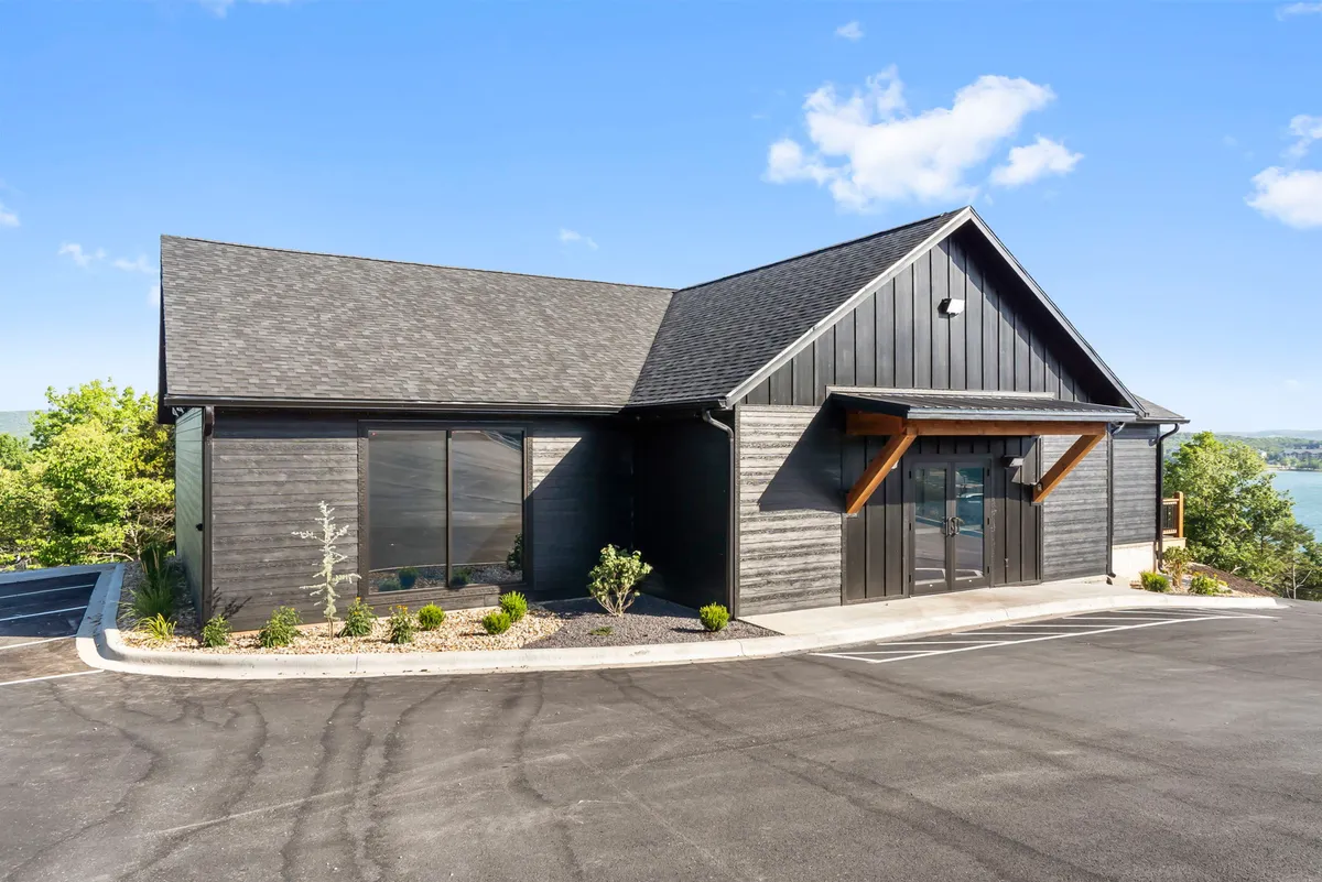 A modern facade featuring large glass windows and wooden accents, set against a stunning natural backdrop. The scene hints at water views and offers a sense of openness and connection to the outdoors.