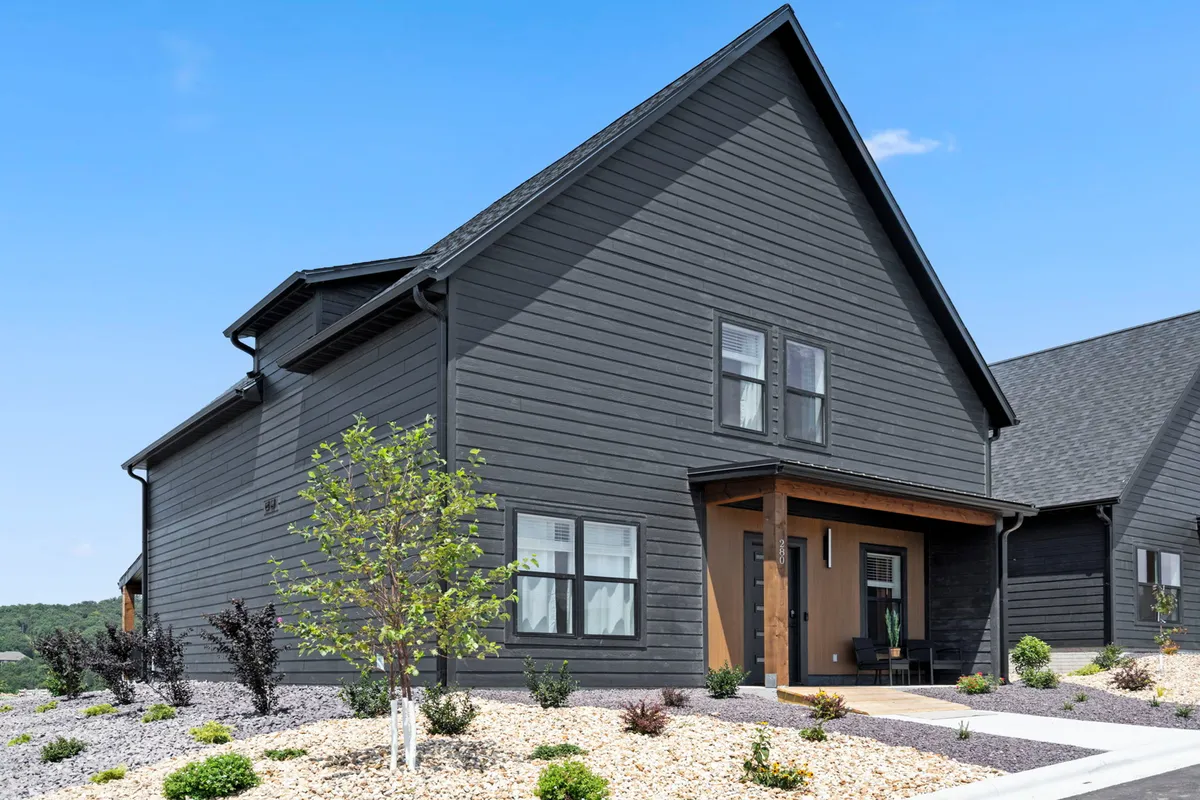 A modern exterior view of the home highlighting clean architecture, a landscaped yard, and a front porch with comfortable seating. The scene suggests easy entry and connection with the outdoors, perfectly inviting for group arrivals or tranquil moments in nature.