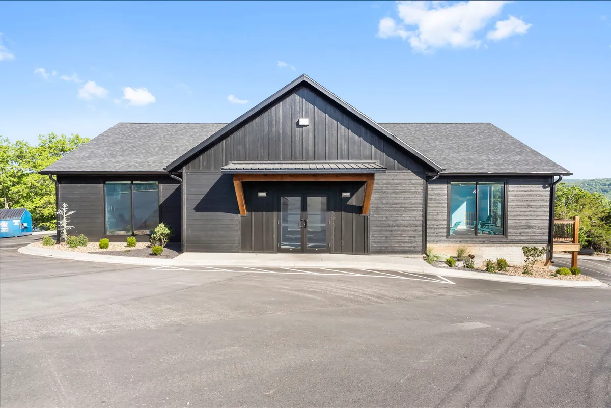 An exterior view highlighting the modern architecture of the retreat, with prominent wood accents, large windows, and landscaped surroundings. The porch is shown as a versatile space for gatherings, celebrations, or enjoying tranquil mornings with coffee, all set against the backdrop of a scenic environment.