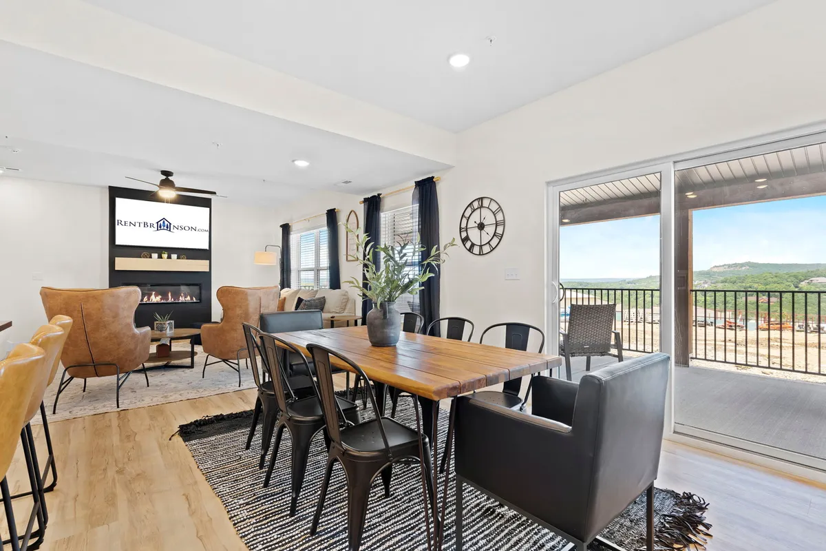 A cozy dining and living area featuring a spacious table for family meals, comfortable seating, a fireplace, and large windows that frame a beautiful view. The setup invites guests to enjoy meals, gather around the fire, and relax together in a warm, inviting environment.