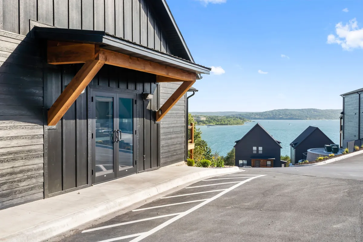 A welcoming exterior shot showing an entrance with wooden accents, a view of the lake in the background, and modern architectural styling. The image highlights both the inviting atmosphere of the retreat and its lakeside setting.